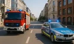 Feuerwehrauto und Polizeiauto fahren mit eingeschaltetem Blaulicht auf einer breiten Stadtstraße zwischen mehrstöckigen Gebäuden.