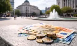 Euro-Münzen und Euro-Banknoten im Vordergrund, dahinter unscharfe moderne Gebäude in Bulgarien als Symbol für den Währungswechsel.