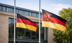 Deutsche Flagge und Flagge von Rheinland-Pfalz auf halbmast vor einem öffentlichen Gebäude bei Tageslicht.
