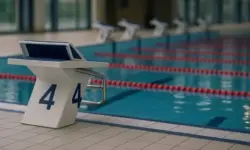 Startblock an einem hellen Indoor-Schwimmbecken mit Wasserbahnen sowie einer Schwimmbrille und Badekappe ohne sichtbare Menschen.