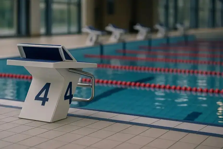 Startblock an einem hellen Indoor-Schwimmbecken mit Wasserbahnen sowie einer Schwimmbrille und Badekappe ohne sichtbare Menschen.