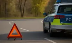 Polizeiauto und aufgestelltes Warndreieck auf einer leeren Landstraße mit herbstlichen Bäumen im Hintergrund.