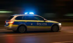 Leere, nächtliche Straße mit Straßenlaternen und leicht glänzendem Asphalt, im Hintergrund diffuse Blaulicht-Reflexe; keine Menschen oder Fahrzeuge sichtbar.