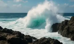 Große Meereswelle, die an einer felsigen Küste bricht, unter klarem Himmel mit starker Gischtbildung.
