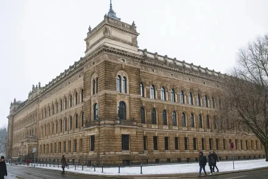 Historisches Gerichtsgebäude in Dresden im Winter, mit Schnee, kahlen Bäumen und einigen vorbeilaufenden Personen auf dem Gehweg.