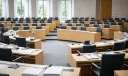 Leerer Plenarsaal eines Landesparlaments mit halbrunder Sitzordnung und gedämpftem Licht, aufgenommen als neutrales Symbol für politische Entscheidungen.