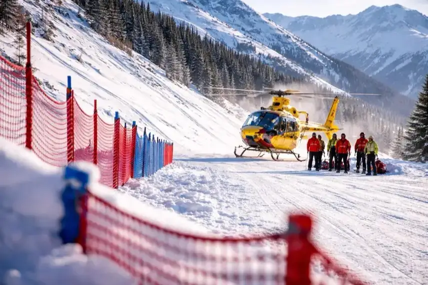 Rettungshubschrauber landet neben verschneiter Weltcup-Abfahrt mit Sicherheitsnetzen und Rettungskräften auf alpiner Skipiste