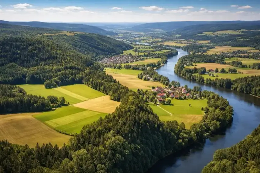 Weitläufige bayerische Landschaft mit Hügeln, Fluss und offenen Feldern, aufgenommen aus erhöhter Perspektive bei klarem Tageslicht.