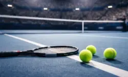 Leerer Hartplatz in einer Tennisarena mit Tennisschläger und Bällen im Vordergrund, unscharfe Tribünen im Hintergrund