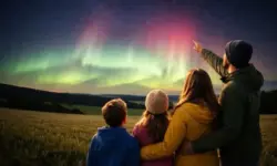 Familie mit Kindern von hinten, der Vater zeigt nach oben auf grünlich leuchtende Polarlichter am hellen Nachthimmel über einer Landschaft