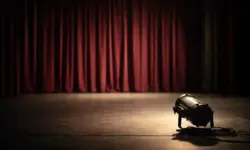 Leere Theaterbühne mit geschlossenem Vorhang und ausgeschaltetem Scheinwerfer, ruhige Bühnenatmosphäre ohne Personen oder Schrift