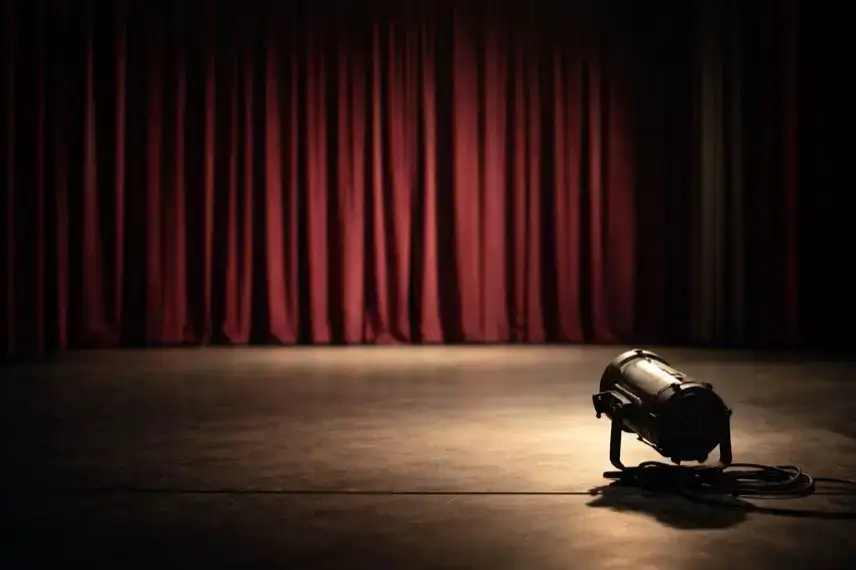 Leere Theaterbühne mit geschlossenem Vorhang und ausgeschaltetem Scheinwerfer, ruhige Bühnenatmosphäre ohne Personen oder Schrift