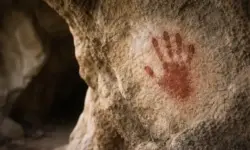 Roter Handabdruck aus Ocker an einer Felswand in einer Kalksteinhöhle in Indonesien, detailreiche Steinstruktur im natürlichen Licht.