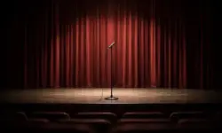 Leere Theaterbühne mit geschlossenem Vorhang und einem einzelnen Mikrofonständer im Vordergrund, neutral beleuchtet, ohne Personen.