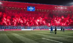 Polizeifahrzeuge und Absperrgitter vor einem Stadion bei Nacht, Rauchschwaden im Hintergrund nach einem Fußballspiel