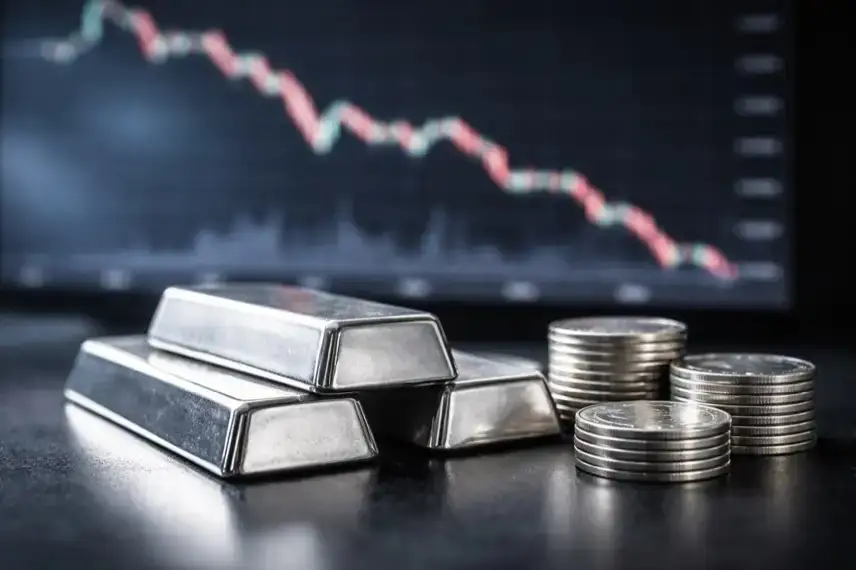 Silberbarren auf dunkler Oberfläche vor unscharfem Börsenchart mit fallender Linie, Darstellung des Silberpreises und der Marktentwicklung