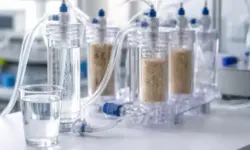 Transparentes Filtersystem zur Trinkwasseraufbereitung mit klaren Schläuchen, Filtermaterial und einem Glas sauberen Wassers im Labor.