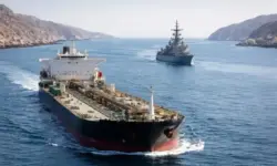 Öltanker und Kriegsschiff fahren durch eine enge Meerenge mit Küstenlinien links und rechts, ruhige See, klarer Himmel.