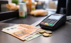 Euro-Banknoten und Münzen neben einem Kartenlesegerät an einer Supermarktkasse als Darstellung von Bargeld und Cashback.