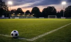 Fußballplatz mit Rasen, Flutlichtmasten und kleiner Tribüne bei Dämmerung, typisch für Spiele in der Oberliga Hamburg