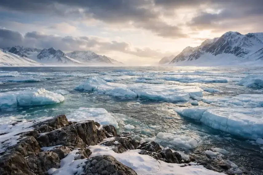 Eisbedeckte Küstenlandschaft in Grönland mit Felsen, Meereseis und bewölktem Himmel in der Arktis