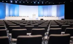 Leere Parteitagshalle mit Reihen von Stühlen und einem Rednerpult, hell ausgeleuchtet, neutrales politisches Veranstaltungsambiente.