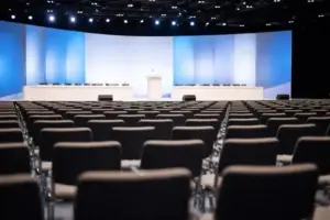 Leere Parteitagshalle mit Reihen von Stühlen und einem Rednerpult, hell ausgeleuchtet, neutrales politisches Veranstaltungsambiente.