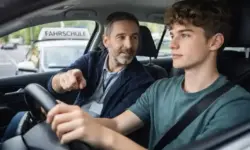 Junger Fahrschüler fährt mit Fahrlehrer in einem Fahrschulauto während einer praktischen Fahrstunde im Straßenverkehr.