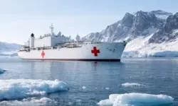 Weißes Lazarettschiff in arktischer See vor Grönland mit Eisflächen und schneebedeckter Küste im Hintergrund