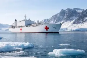 Weißes Lazarettschiff in arktischer See vor Grönland mit Eisflächen und schneebedeckter Küste im Hintergrund