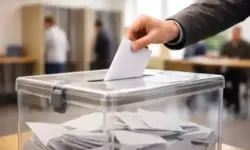 Stimmzettel wird in Wahlurne eingeworfen in einem Wahllokal bei einer Landtagswahl in Deutschland mit Wahlkabinen im Hintergrund